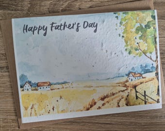 Può includere: Un biglietto per la festa del papà ad acquerello con un paesaggio rurale con case, campi e un albero. Il biglietto riporta la scritta "Happy Father's Day" in stile manoscritto. Il biglietto è posto su una busta marrone.