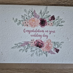 Könnte beinhalten: Hochzeitskarte mit floralem Design. Die Karte zeigt eine aquarellartige Anordnung von rosa und burgunderfarbenen Blumen mit grünen Blättern. Der Text "Glückwunsch zu Ihrem Hochzeitstag" ist in Schreibschrift geschrieben.