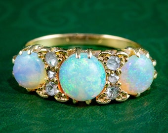 May include: A gold ring with three opal gemstones and small diamond accents. The ring is set in a delicate, ornate design.