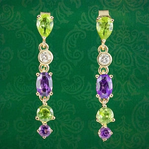 May include: A pair of gold earrings with green and purple gemstones. The earrings have a pear-shaped green stone at the top, followed by a round white stone, then an oval purple stone, a round green stone, and a smaller oval purple stone at the bottom.