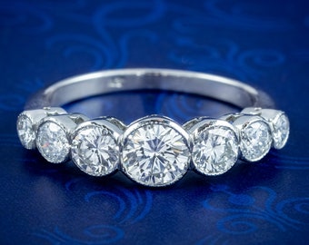 May include: A silver band with a row of seven round, bezel-set diamonds. The diamonds are graduated in size, with the largest diamond in the center.