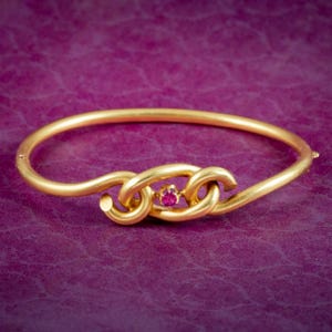 Puede incluir: Un brazalete de oro con una piedra preciosa de rubí engastada en el centro de un diseño retorcido.