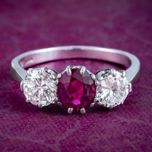 May include: A silver ring with a large oval ruby surrounded by two smaller round diamonds.