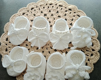 May include: A set of seven crocheted baby booties in white with different embellishments, including bows and pearl accents. The booties are arranged on a beige crocheted doily. The text "PDF PATTERN GET 4 STYLES PATTERN" is at the top of the image. The text "Made by Thanunnuda" is at the bottom of the image.