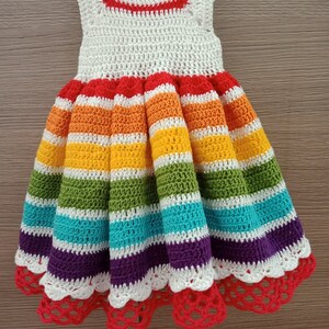 May include: A rainbow striped crochet dress with a white crochet bodice and a white crochet lace trim. The dress has a red crochet band at the neckline and a red crochet band at the hem.