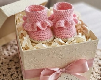May include: A pair of light pink crocheted baby booties with ruffled cuffs, presented inside a cream-colored gift box with a pink ribbon and a tag that reads For baby, with love. The text PDF PATTERN is visible at the top of the image.
