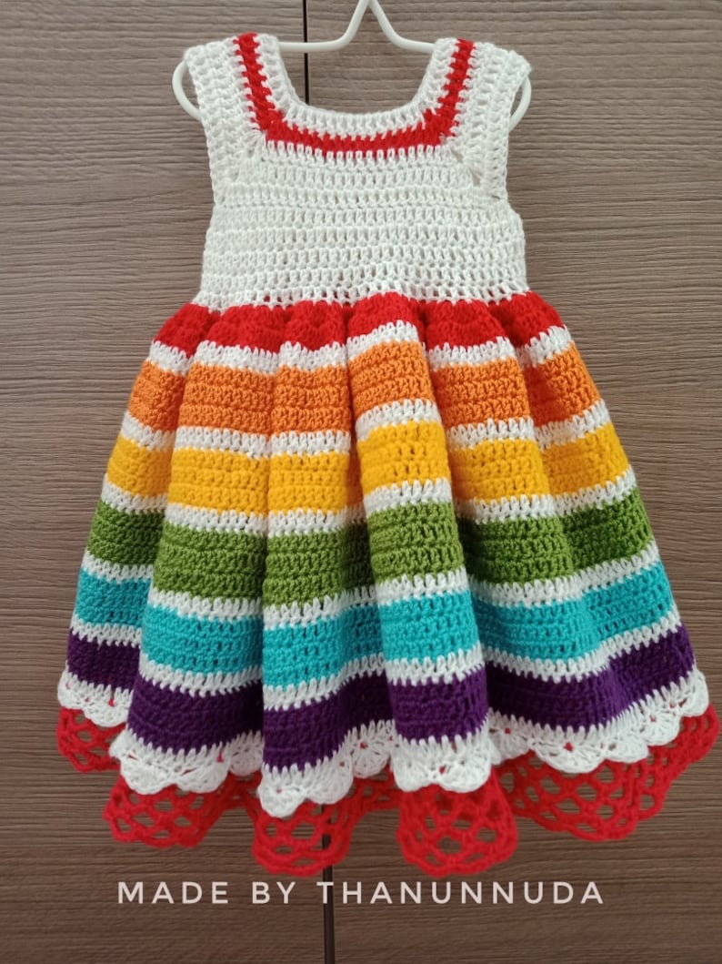 May include: A white crochet dress with rainbow stripes and a red crochet trim. The dress has a scalloped hem and is made with a fine yarn.