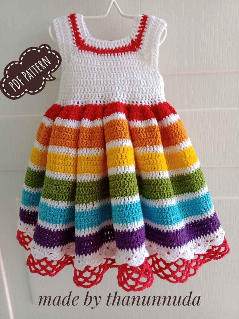 May include: A white crochet dress with rainbow stripes and a red crocheted trim. The dress has a scalloped hem with a white and red crocheted border. The dress is made by thanunnuda.