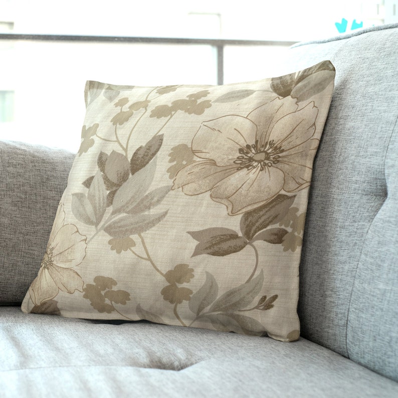 May include: A beige throw pillow with a floral pattern in shades of brown. The pillow features a large flower with a brown center and smaller flowers and leaves throughout the design.