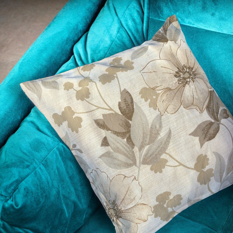 May include: A white throw pillow with a floral pattern in shades of brown and beige, resting on a teal blue couch.