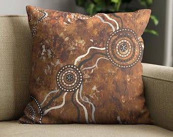 May include: A square throw pillow featuring a textured, mottled brown background with a printed design of two large concentric circles connected by wavy white and grey lines, accented with small white dots throughout the pattern.