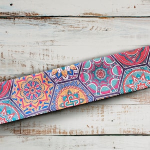May include: A colourful patterned fabric with a repeating design of geometric shapes and floral motifs. The fabric is a mix of pink, blue, yellow, and green colours.