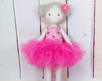 Puede incluir: Una muñeca hecha a mano con una falda de tul rosa y un corpiño de encaje blanco. La muñeca tiene una flor rosa en el pelo y una cara blanca.