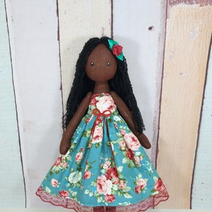 black fabric doll with long yarn hair in a green dress that can be removed and replaced with another