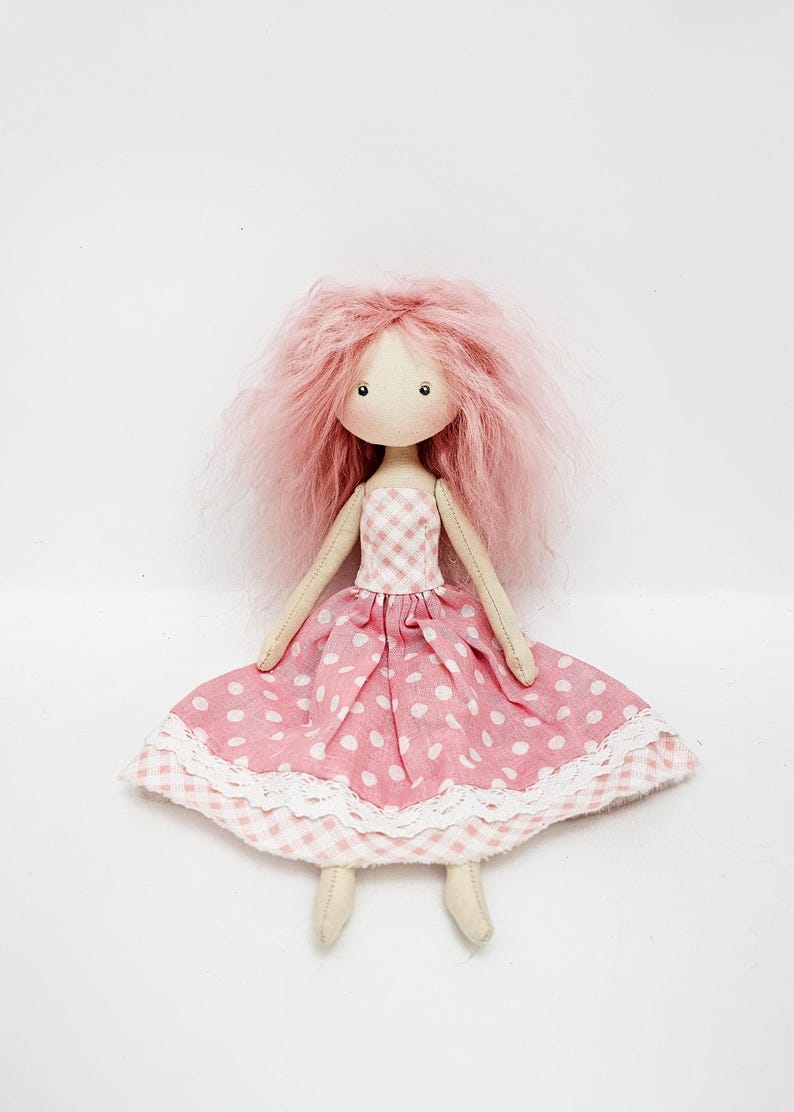May include: A handmade doll with pink yarn hair, wearing a pink and white gingham dress with white polka dots and a white lace trim.
