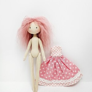 May include: A handmade doll with pink yarn hair and a pink and white polka dot dress. The doll has a simple, sewn-on face with black eyes and a pink mouth.