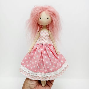 May include: A handmade doll with pink yarn hair, wearing a pink and white gingham dress with white polka dots and a white lace trim.
