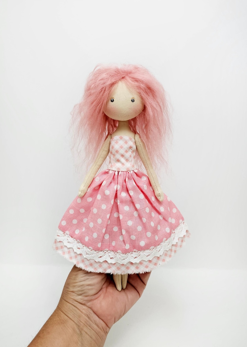 May include: A handmade doll with pink yarn hair, wearing a pink and white gingham dress with white polka dots and a white lace trim.