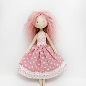 May include: A handmade pink fabric doll with pink and white polka dot dress and a white lace trim. The doll has pink yarn hair.