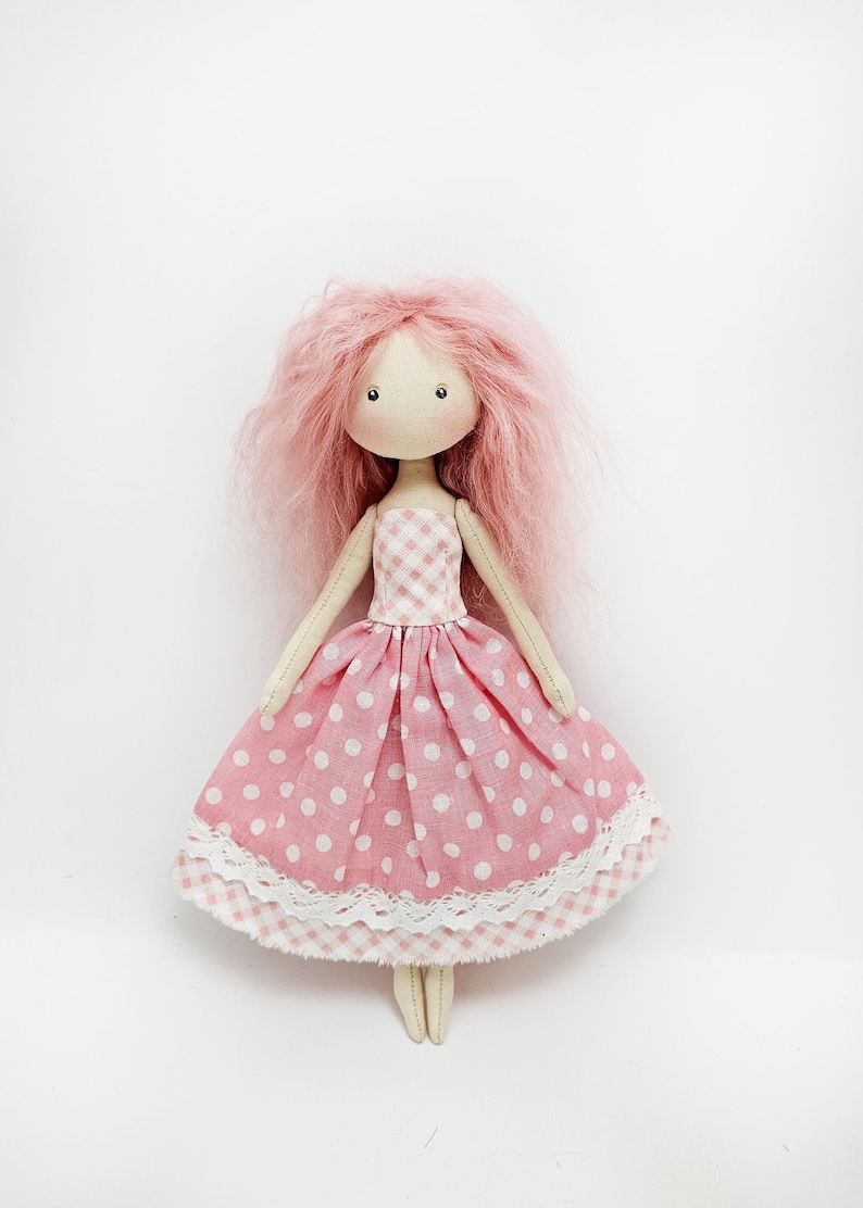 May include: A handmade pink fabric doll with pink and white polka dot dress and a white lace trim. The doll has pink yarn hair.