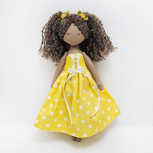 May include: A handmade doll with brown curly hair, wearing a yellow dress with white polka dots and yellow buttons.