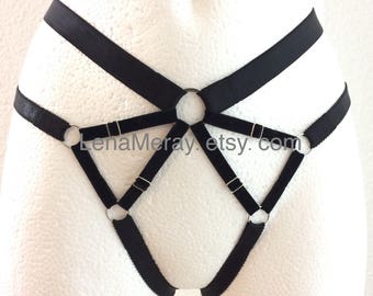 May include: Black lingerie harness with silver metal rings. The harness has a geometric design with multiple straps and rings.