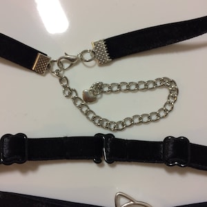 May include: A set of four black velvet choker necklaces with silver metal clasps and charms. One charm is a heart, another is a cat head, and the other two are simple circles.
