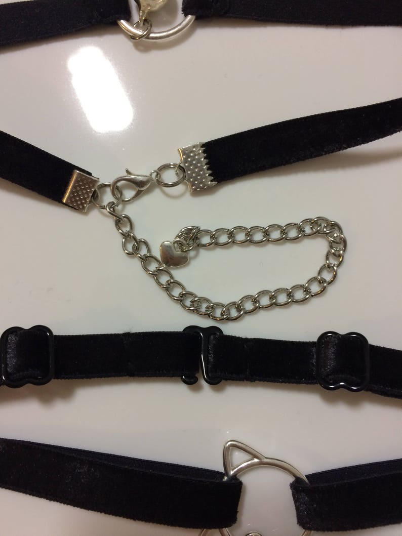 May include: A set of four black velvet choker necklaces with silver metal clasps and charms. One charm is a heart, another is a cat head, and the other two are simple circles.