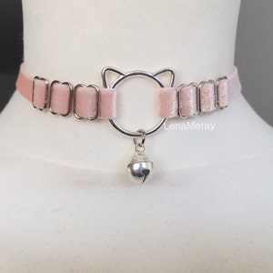 May include: A pink velvet choker with a silver cat-shaped charm and a bell pendant.