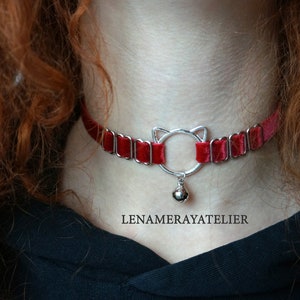 May include: A red velvet choker with a silver cat-shaped charm and a bell. The choker is adjustable and has a delicate, feminine look.