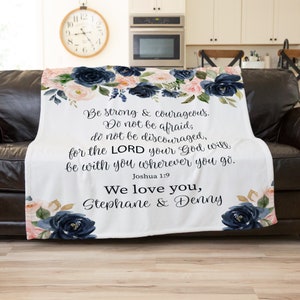 May include: White throw blanket with a navy blue and pink floral design. The blanket features a bible verse from Joshua 1:9, "Be strong & courageous. Do not be afraid; do not be discouraged, for the LORD your God will be with you wherever you go." The blanket is personalized with the text "We love you, Stephane & Denny".