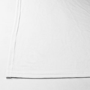 May include: A plain white fabric with a single seam running down the side and a black seam along the bottom edge.