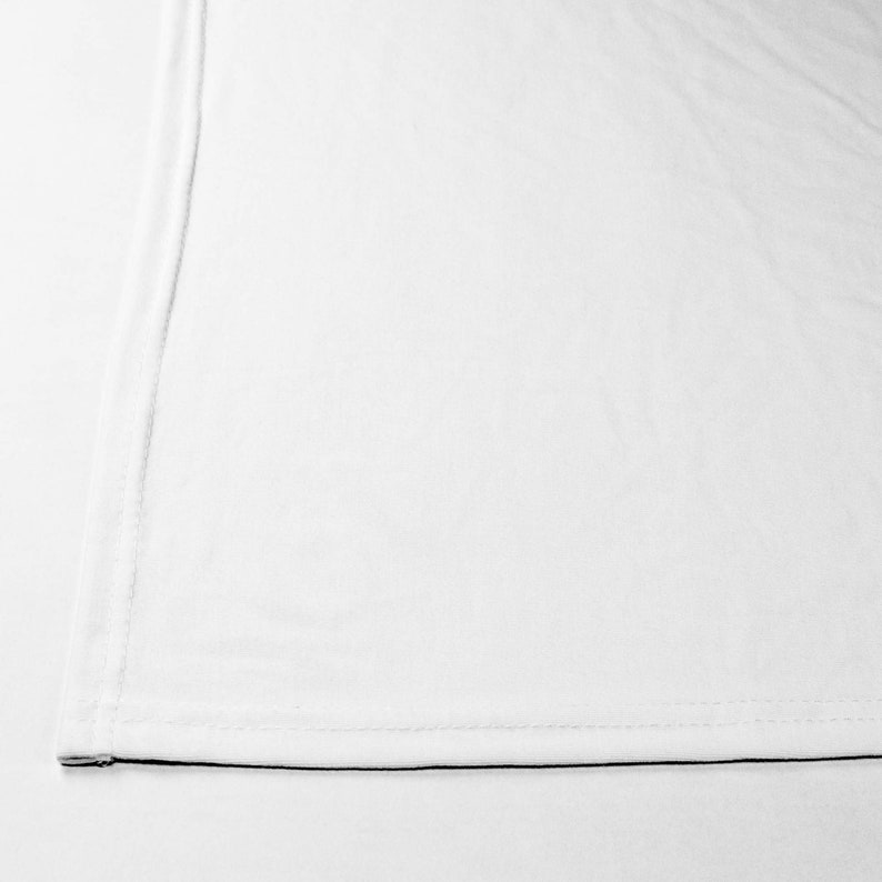 May include: A plain white fabric with a single seam running down the side and a black seam along the bottom edge.