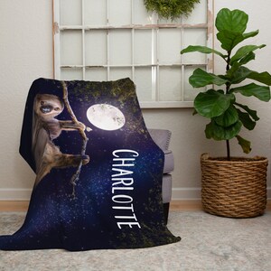 May include: A soft, blue fleece blanket featuring a sloth hanging from a branch in front of a full moon. The blanket has a starry night background and the name "Charlotte" printed on the side.