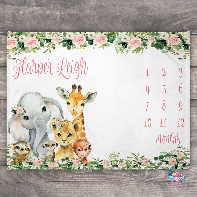 May include: A white baby blanket with a floral border and a watercolor illustration of a giraffe, elephant, lion, monkey, and sloth. The blanket also has the name "Harper Leigh" and a chart for tracking a baby's growth in months.