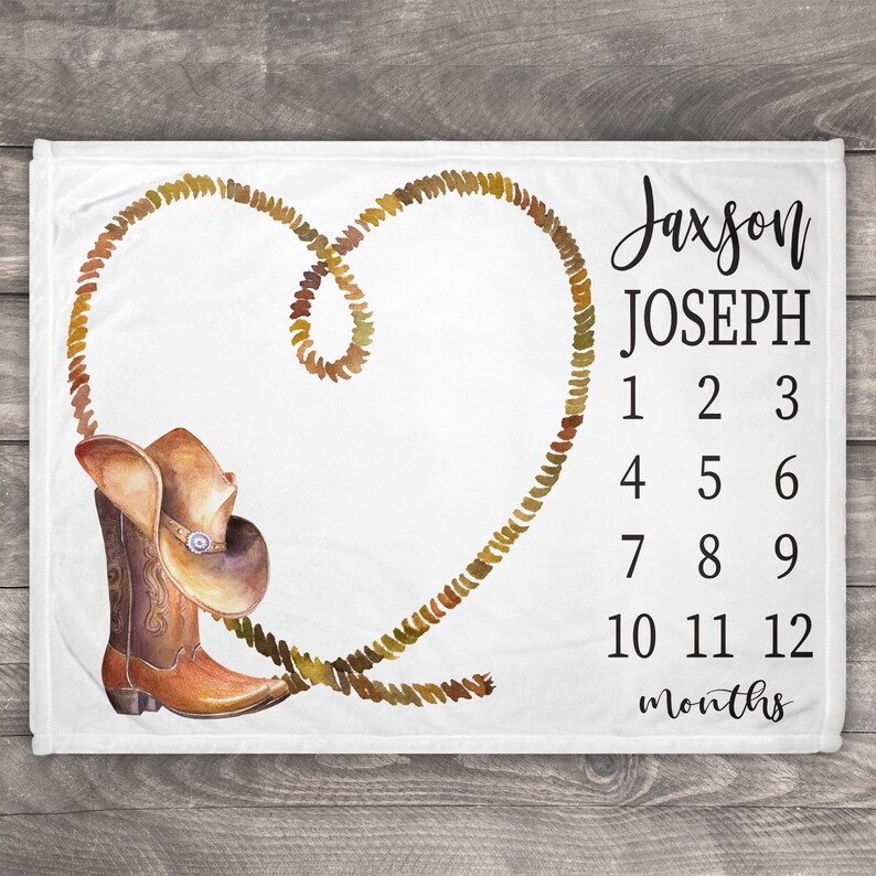 May include: A white baby blanket with a brown cowboy boot and hat, a brown rope in the shape of a heart, and the text "Jaxson JOSEPH 1 2 3 4 5 6 7 8 9 10 11 12 months".