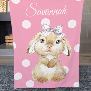 Op de afbeelding: Een roze fleece deken met witte stippen en een bruin konijn met een roze strik. De deken heeft de naam "Savannah" erop.