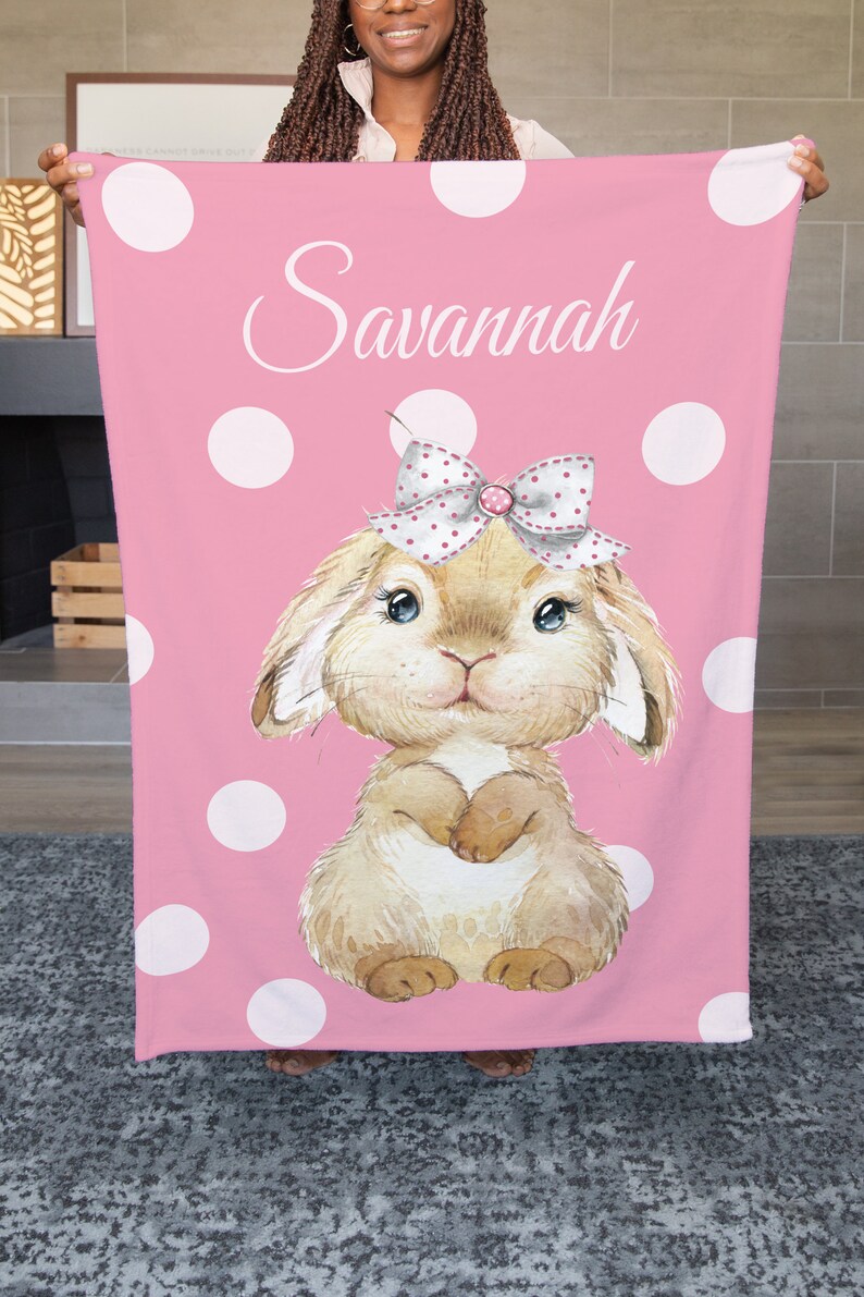 Op de afbeelding: Een roze fleece deken met witte stippen en een bruin konijn met een roze strik. De deken heeft de naam "Savannah" erop.
