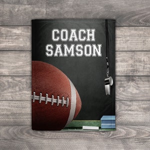 Pu&ograve; includere: Una lavagna nera con il testo "COACH SAMSON" scritto in bianco. Un pallone da football marrone e bianco &egrave; sul lato sinistro della lavagna. Un fischietto &egrave; appeso a una corda nera sul lato destro della lavagna.