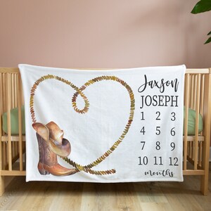 May include: White baby blanket with a brown cowboy boot and hat design. A rope is shaped into a heart with the text "Jaxson Joseph" and numbers 1-12 for each month.