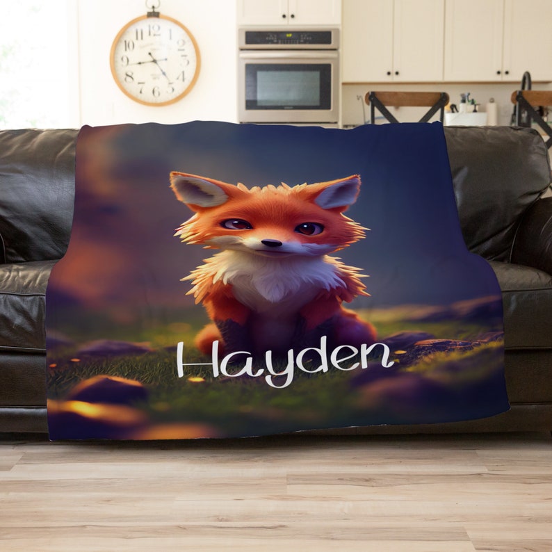 May include: A soft blanket with a cartoon fox design. The fox has orange and white fur and is set against a blurred forest backdrop. The name "Hayden" is written in white script on the blanket.