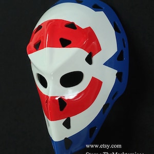 K&ouml;nnte beinhalten: Eine wei&szlig;e Hockey-Torwartmaske mit rotem und blauem Design. Die Maske hat ein gro&szlig;es "C" auf der Vorderseite, mit einem roten Streifen dar&uuml;ber und einem blauen Streifen darunter. Die Maske hat ein schwarzes Visier und einen schwarzen Kinnriemen. www.etsy.com Store: TheMaskterpiece