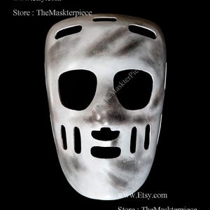 May include: A silver hockey mask with black shading and cut-out eye holes, mouth, and ventilation slots. The mask has a distressed, weathered appearance. The Etsy store name and website are visible at the bottom of the image.