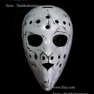 May include: A white hockey mask with black cracked paint and a black nose. The mask has a series of small holes around the eyes and mouth.