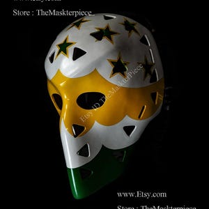 Könnte beinhalten: Eine weiße, gelbe und grüne Hockey-Torwartmaske mit einem Sternendesign. Die Maske hat einen weißen Hintergrund mit gelben und grünen Akzenten. Die Sterne sind grün mit schwarzen Umrissen. Der Text "Etsy ID TheMaskterpiece" ist auf der Maske geschrieben.