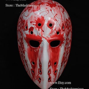 Könnte beinhalten: Weiße Hockeymaske mit roten Farbspritzern. Die Maske hat eine Reihe von Löchern um die Augen und den Mund. Der Text "www.etsy.com Store: TheMaskterpiece" ist am unteren Rand des Bildes sichtbar.