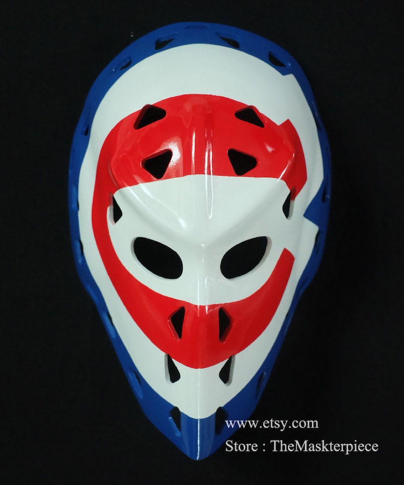 K&ouml;nnte beinhalten: Eine wei&szlig;e Hockey-Torwartmaske mit rotem und blauem Design. Die Maske hat ein gro&szlig;es "C" auf der Vorderseite, mit einem roten Streifen oben und einem blauen Streifen unten. Die Maske hat eine Reihe von L&ouml;chern zur Bel&uuml;ftung.