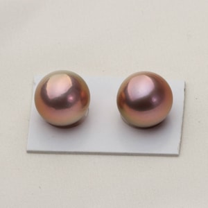 May include: Two round, iridescent pink pearls on a white background.