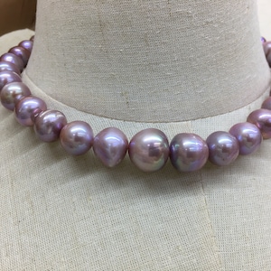 Może przedstawiać: Naszyjnik wykonany z dużych, okrągłych, lawendowych pereł. Perły są nawleczone na cienki, srebrny łańcuszek.