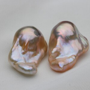 Può includere: Due perle barocche con una finitura iridescente e madreperlacea. Le perle sono di colore rosa chiaro e bianco.